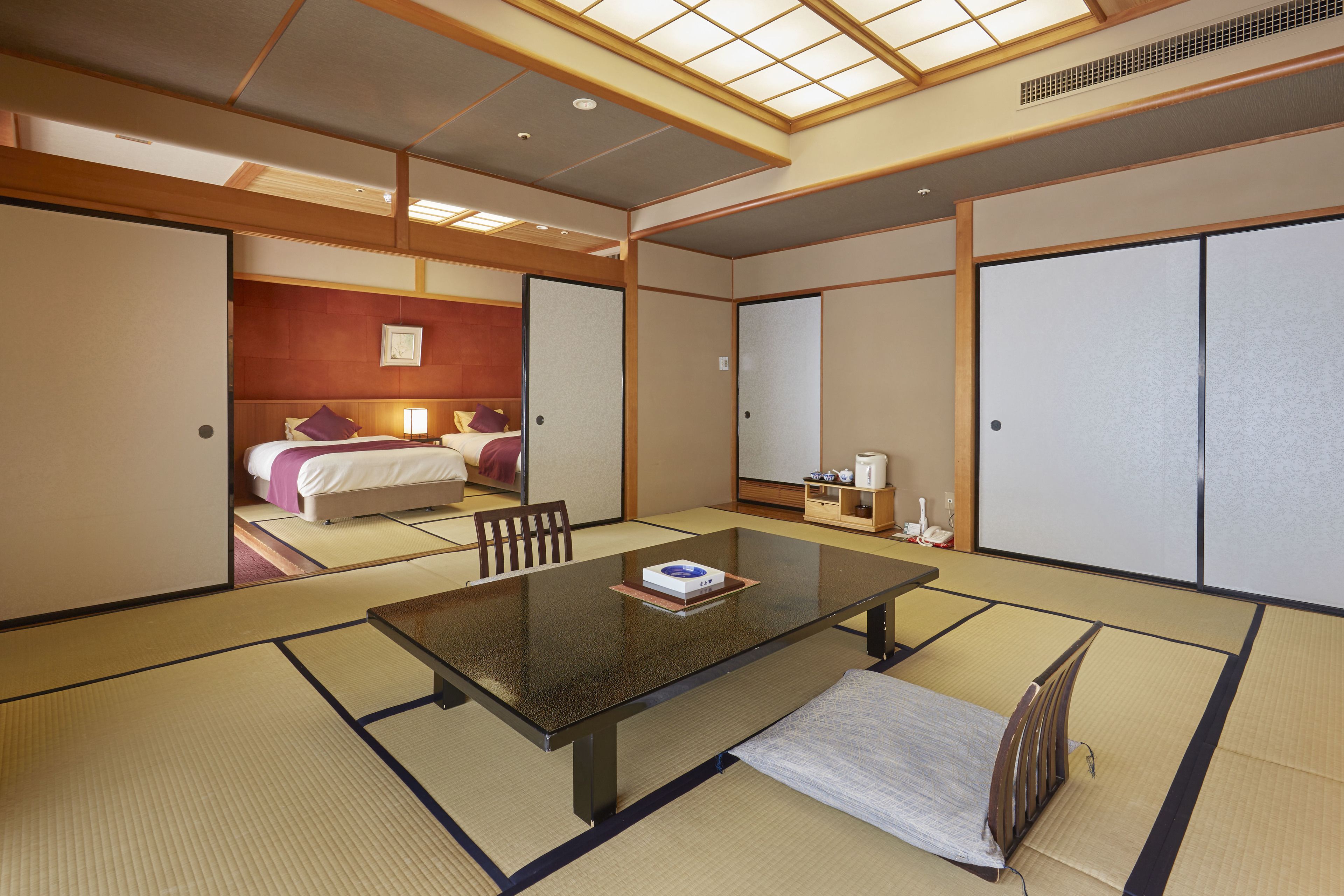 A traditional Japanese-style room with tatami flooring, a low table, and a bed with a wooden headboard.