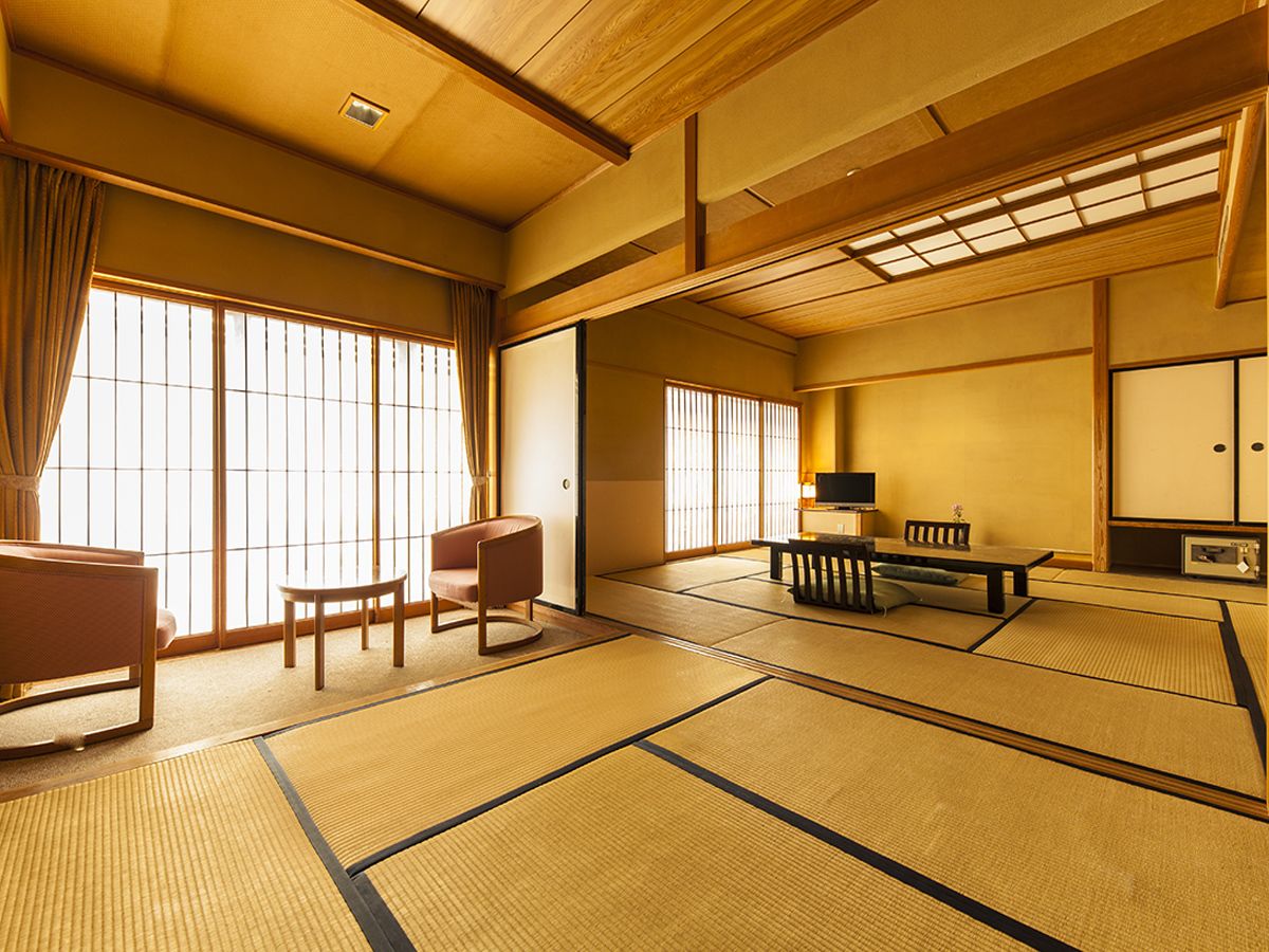 A traditional Japanese room with tatami flooring, sliding doors, a low table with cushions, and a television.