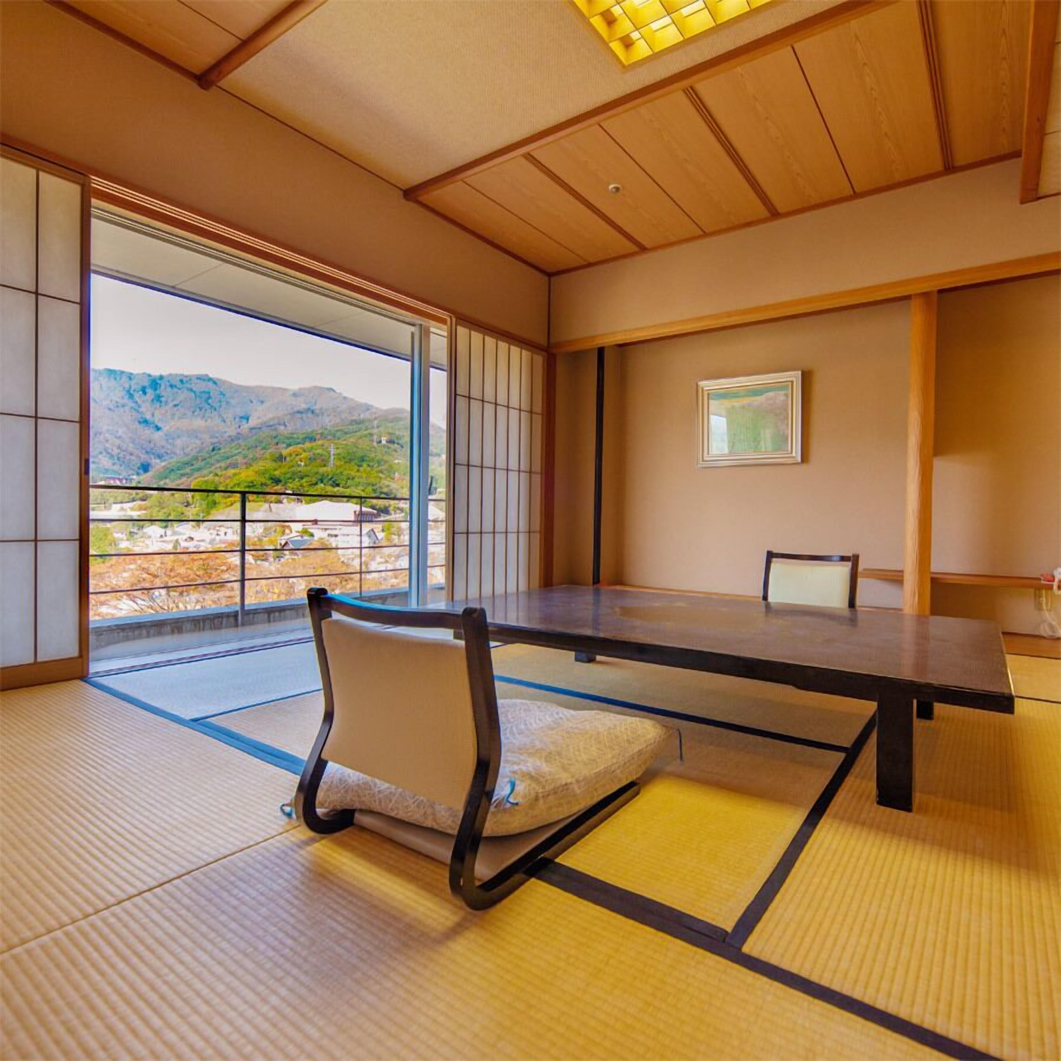 A traditional Japanese room with tatami flooring, a low table, and a view of mountains.