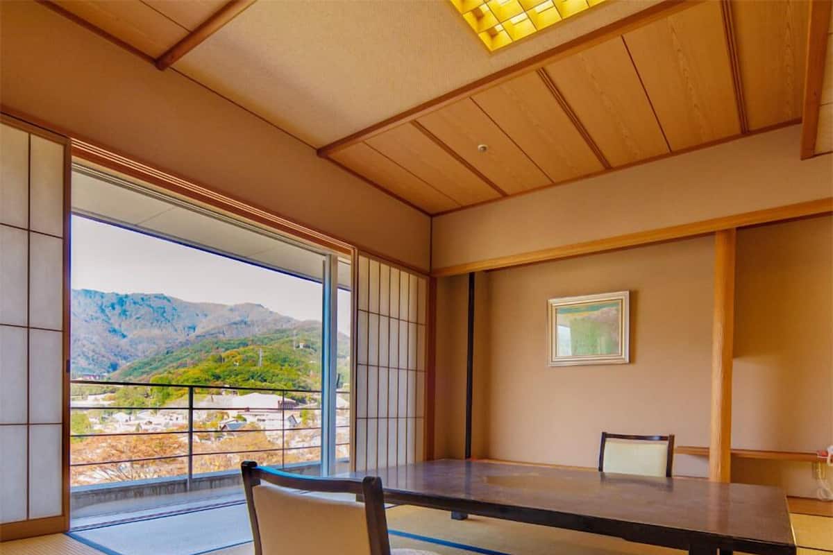 A traditional Japanese room with tatami flooring, a low table, and a view of mountains.