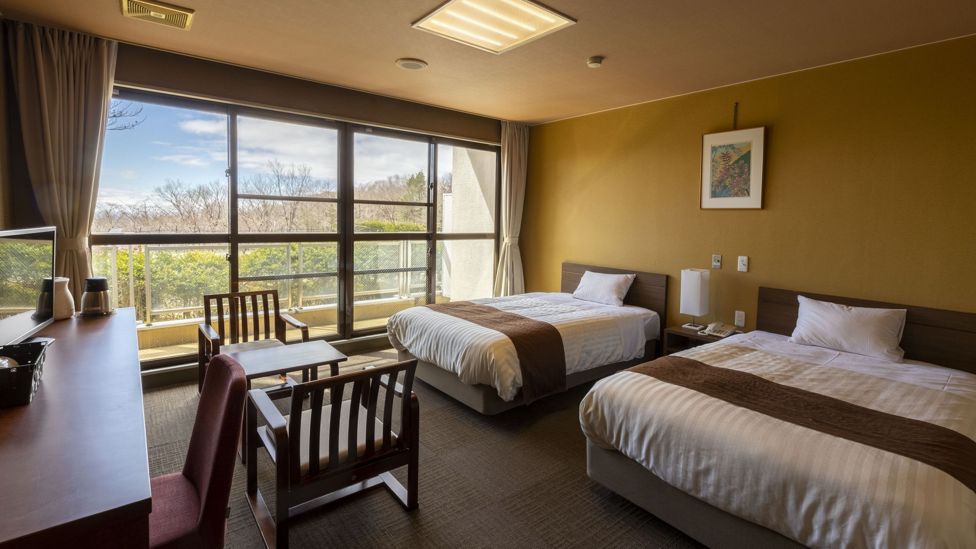 A hotel room with two beds, a desk, a chair, a window with a view, and a painting on the wall.