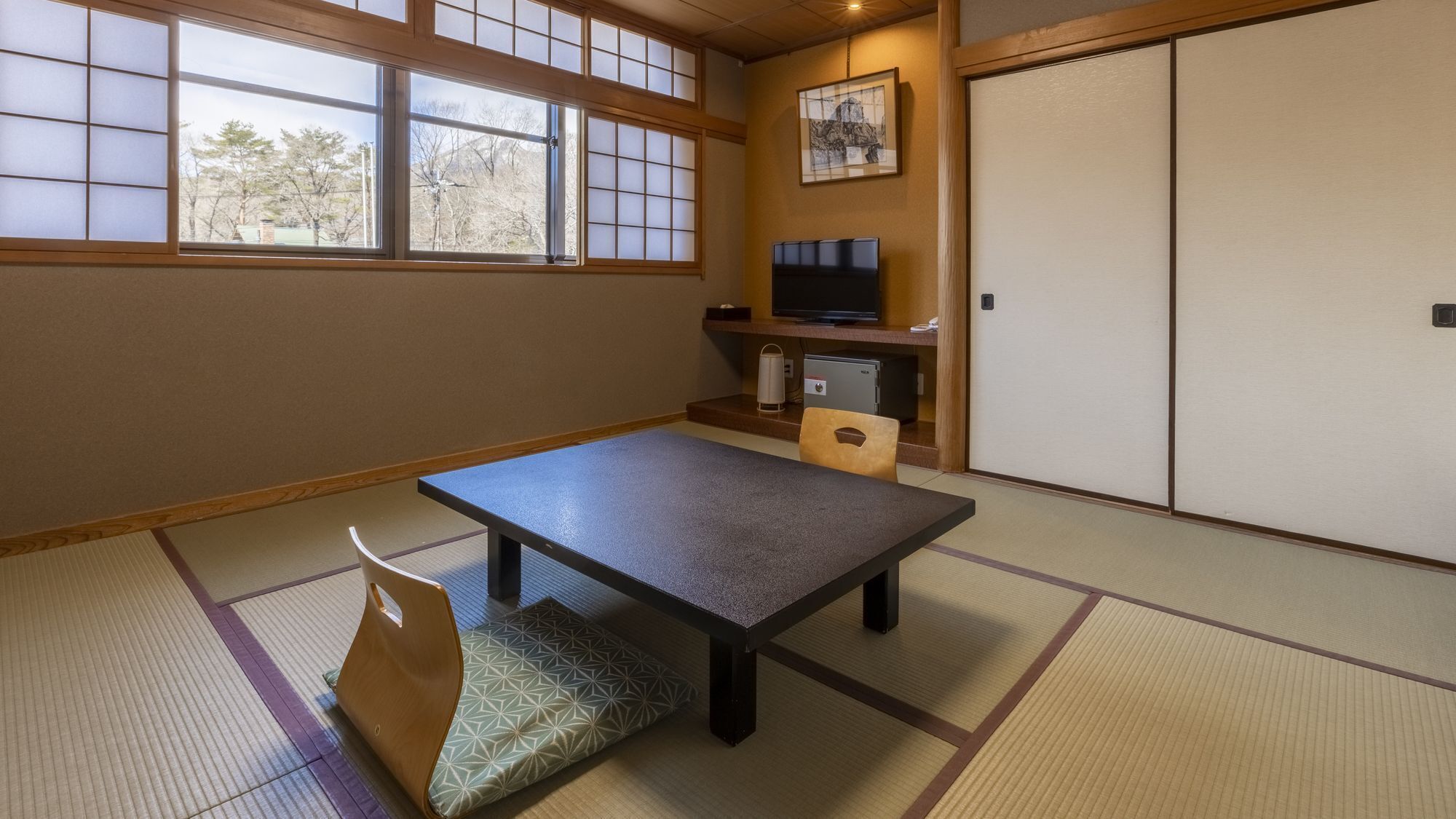 A traditional Japanese room with tatami flooring, a low table, a cushioned bench, a television, and a sliding door.