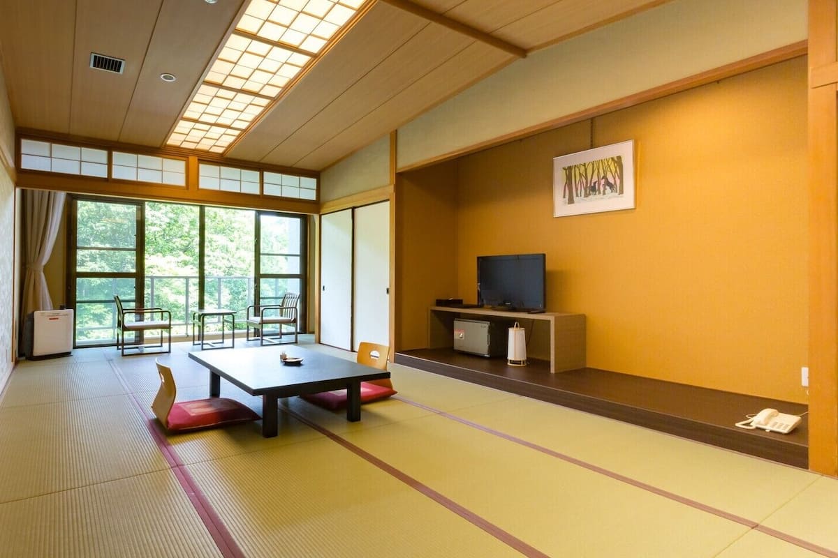 Una habitación con suelo de tatami, una mesa baja, sillas, un televisor y un mueble pequeño.