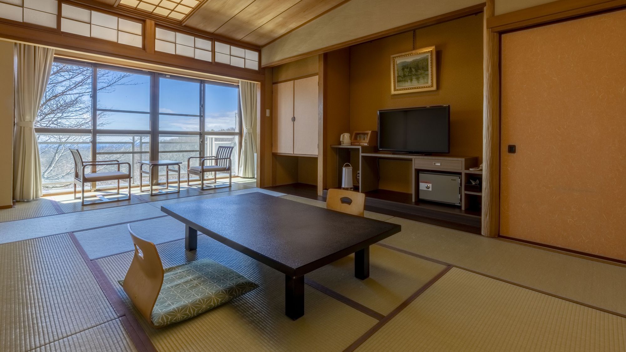 A traditional Japanese room with tatami flooring, a low table, chairs, a television, and a view of the outdoors.