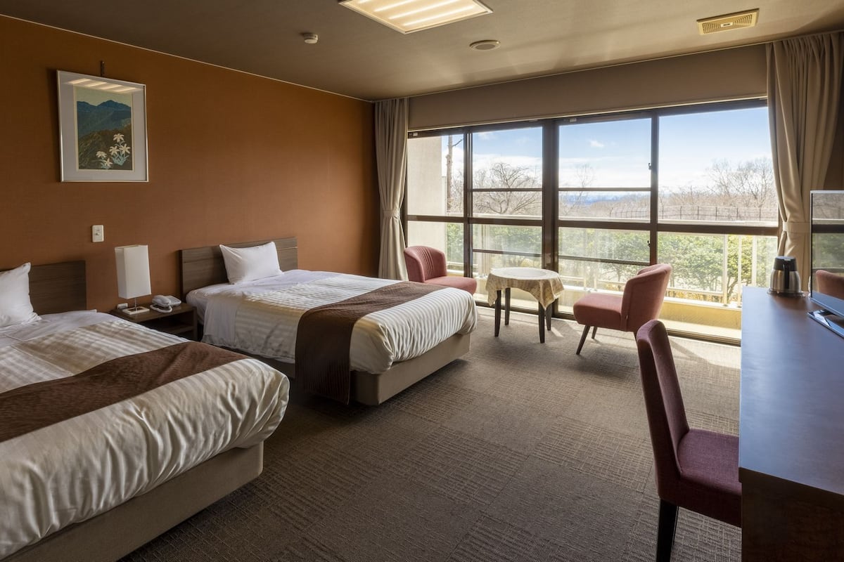 Habitación de hotel con dos camas, un escritorio, una silla, una mesita y un ventanal grande con vistas.