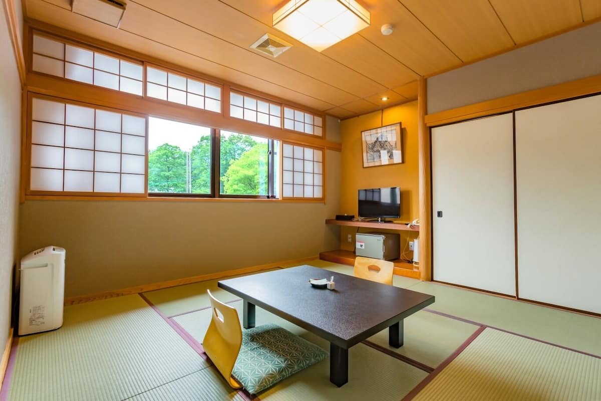 Una habitación japonesa tradicional con suelo de tatami, una mesa baja, un televisor y una puerta corredera.