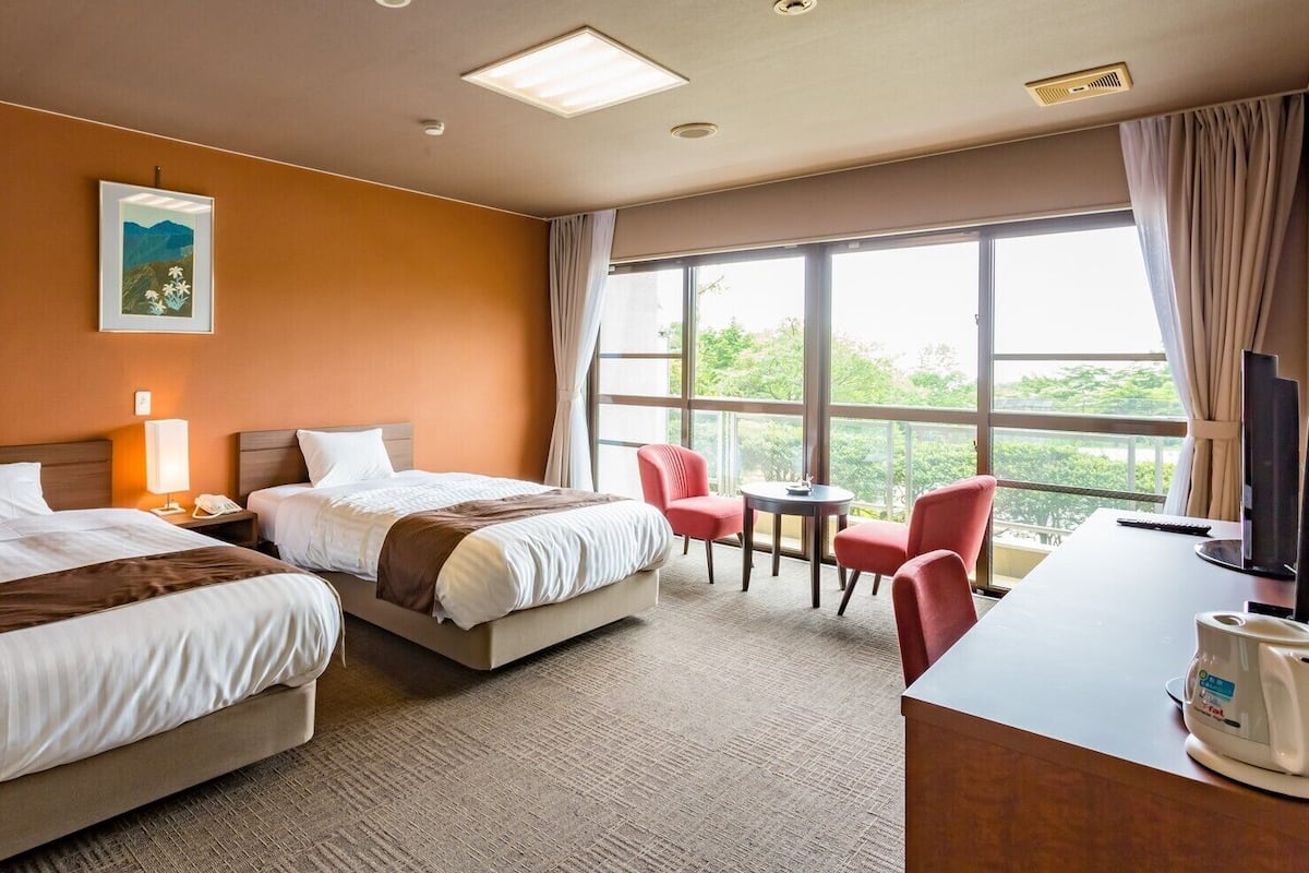 Habitación de hotel con dos camas, un escritorio, una silla, un televisor y una ventana con vistas.