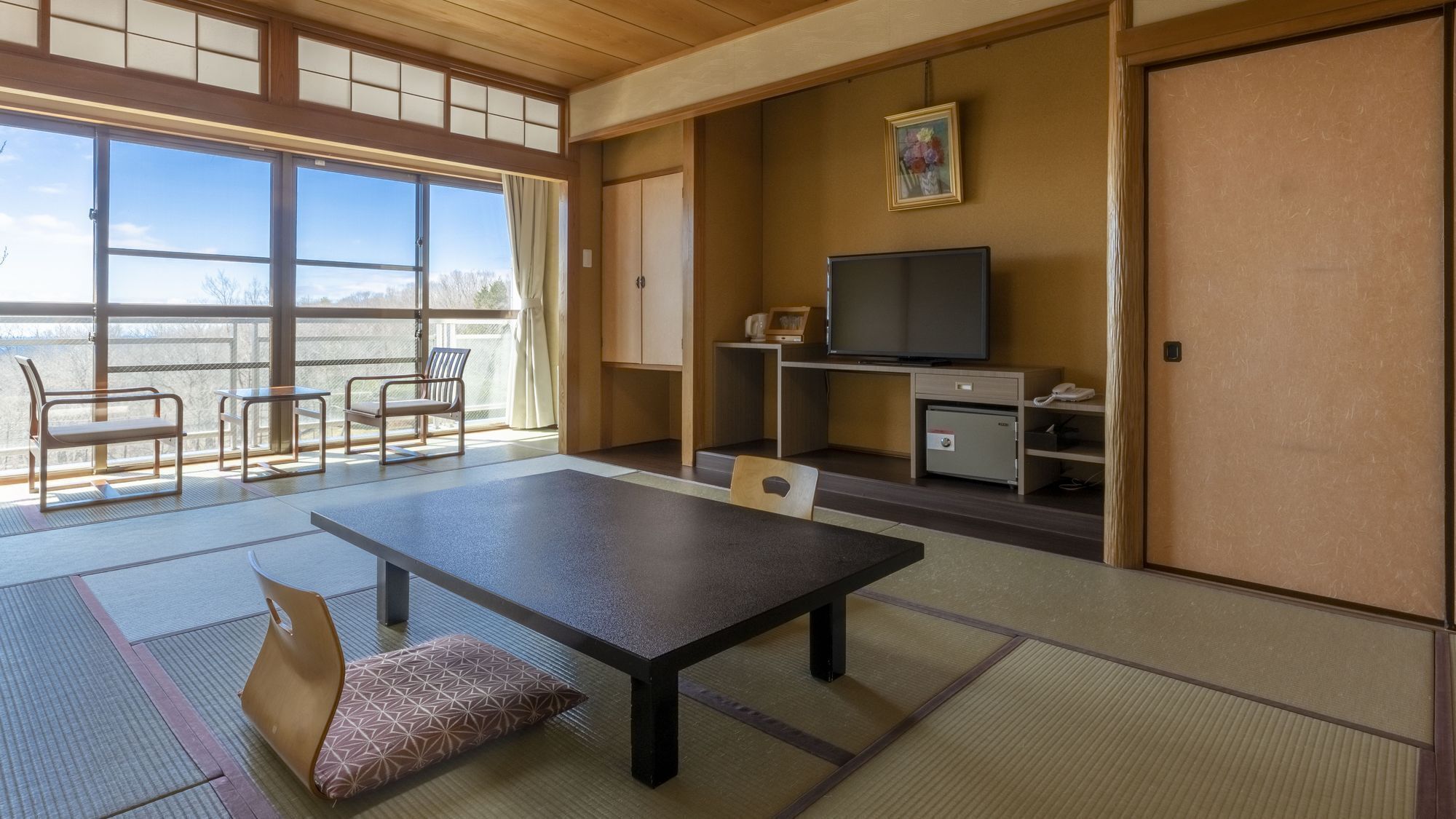 A traditional Japanese-style room with tatami flooring, a low table, chairs, a television, a safe, and a sliding door.