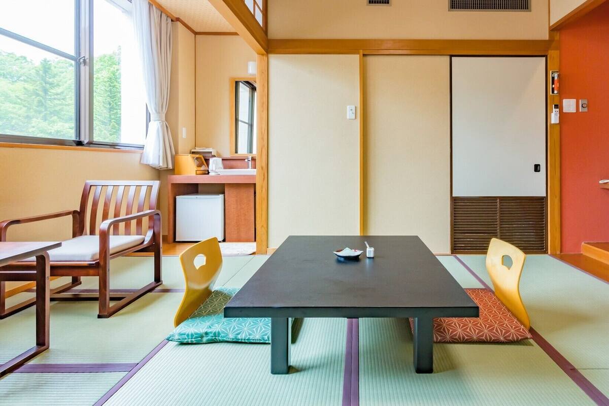 Una habitación japonesa tradicional con suelo de tatami, una mesa baja, sillas, un televisor y una puerta corrediza.