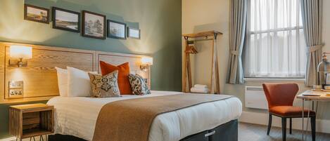 A neatly arranged hotel room with a bed, bedside tables, a chair, and a window with curtains.