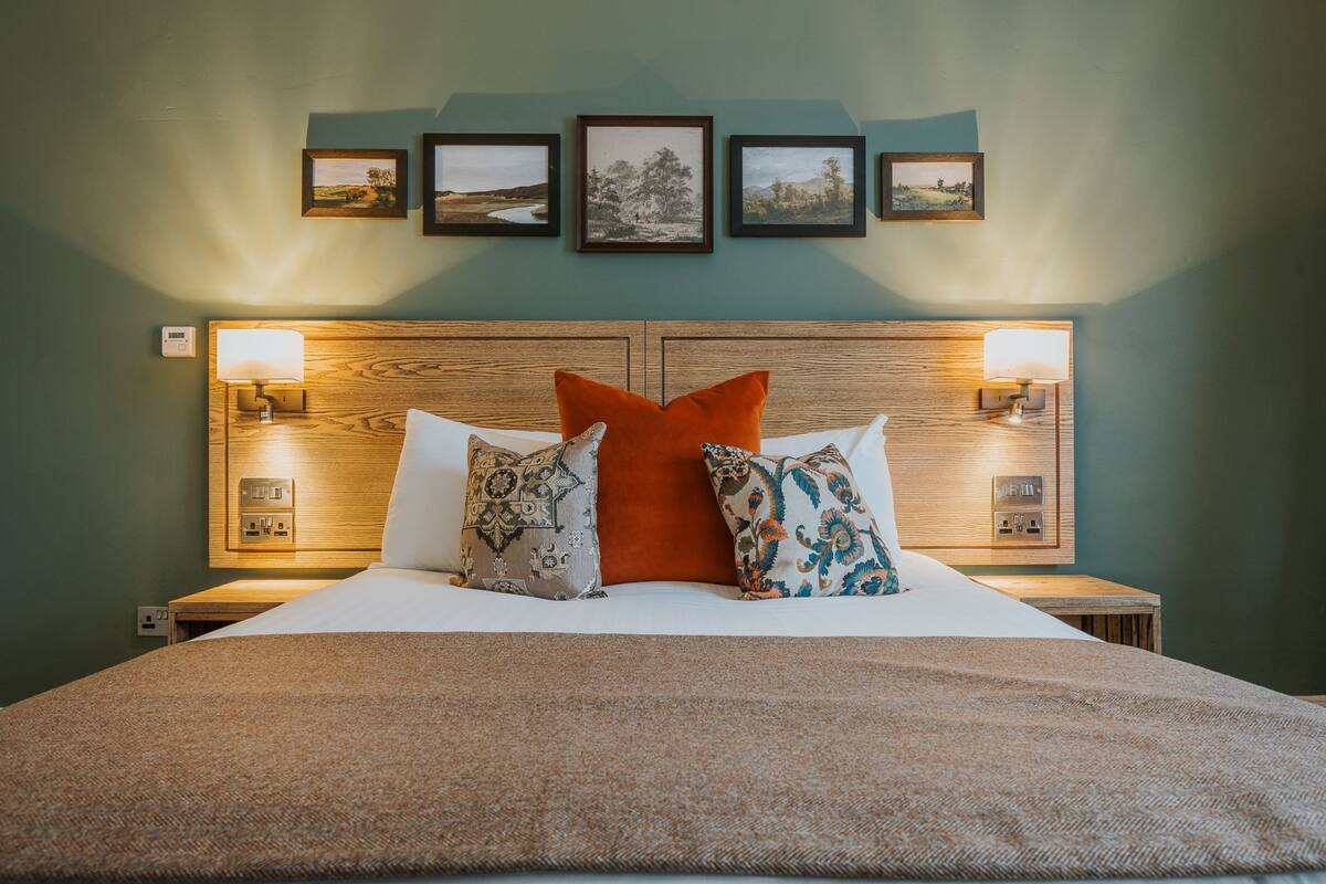 A neatly made bed with a brown blanket, two nightstands with lamps, and four framed pictures on the wall.