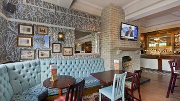 A bar area with a stone fireplace, a television mounted on the wall, and a bar stocked with bottles.