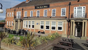 A traditional brick building with a sign reading 'The Blue Bell Hotel.' It features a covered outdoor seating area with wooden tables and chairs, and a planter with various plants. - The Blue Bell (Middlesbrough)