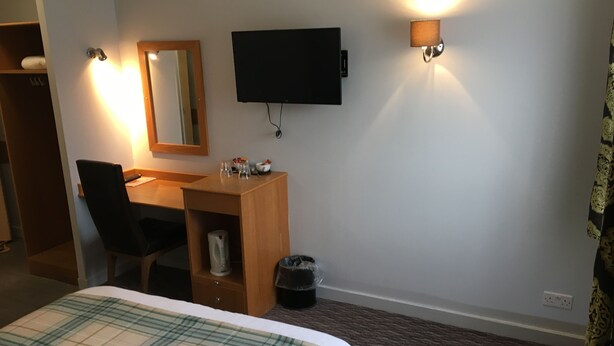 A hotel room with a bed, a desk, a chair, a TV, and a trash bin. - The Blue Bell (Middlesbrough)