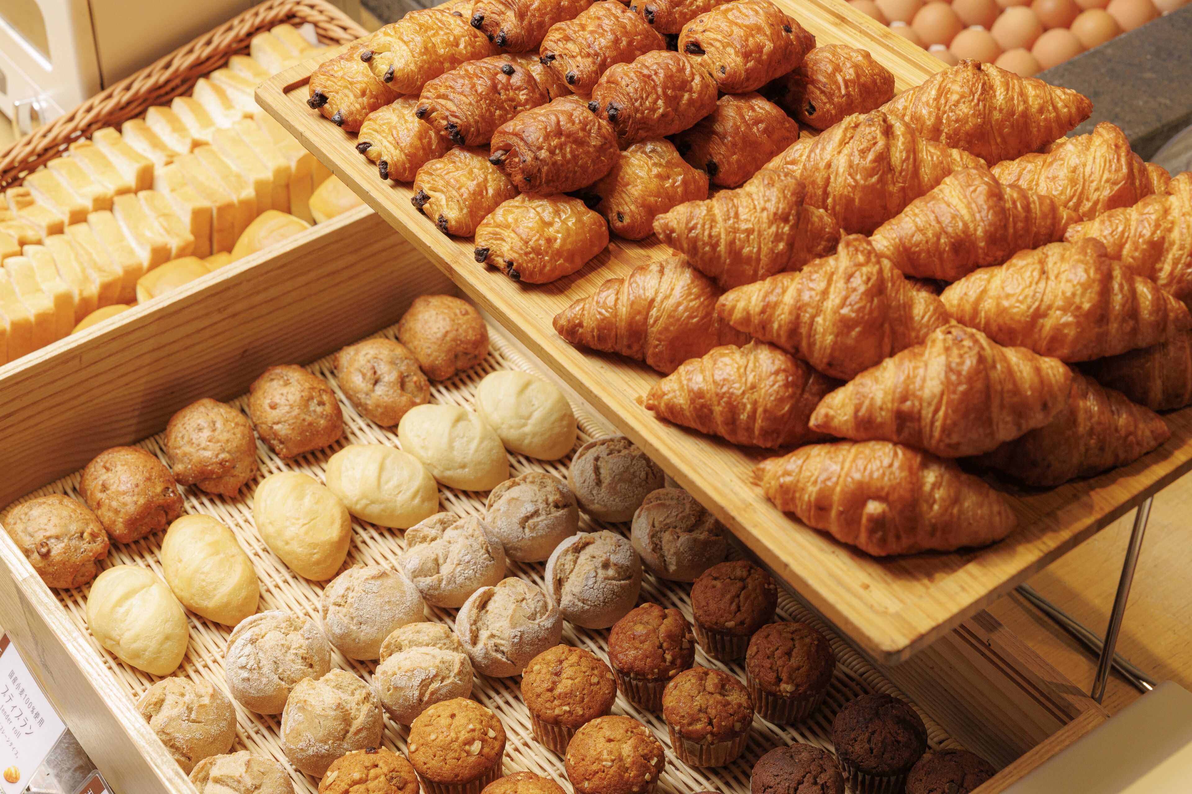 Mostrador de panadería con diversos productos horneados, incluyendo croissants, muffins y pan.