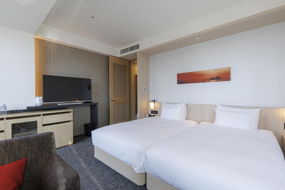 A hotel room with a large bed, a TV, a desk, and a painting on the wall.