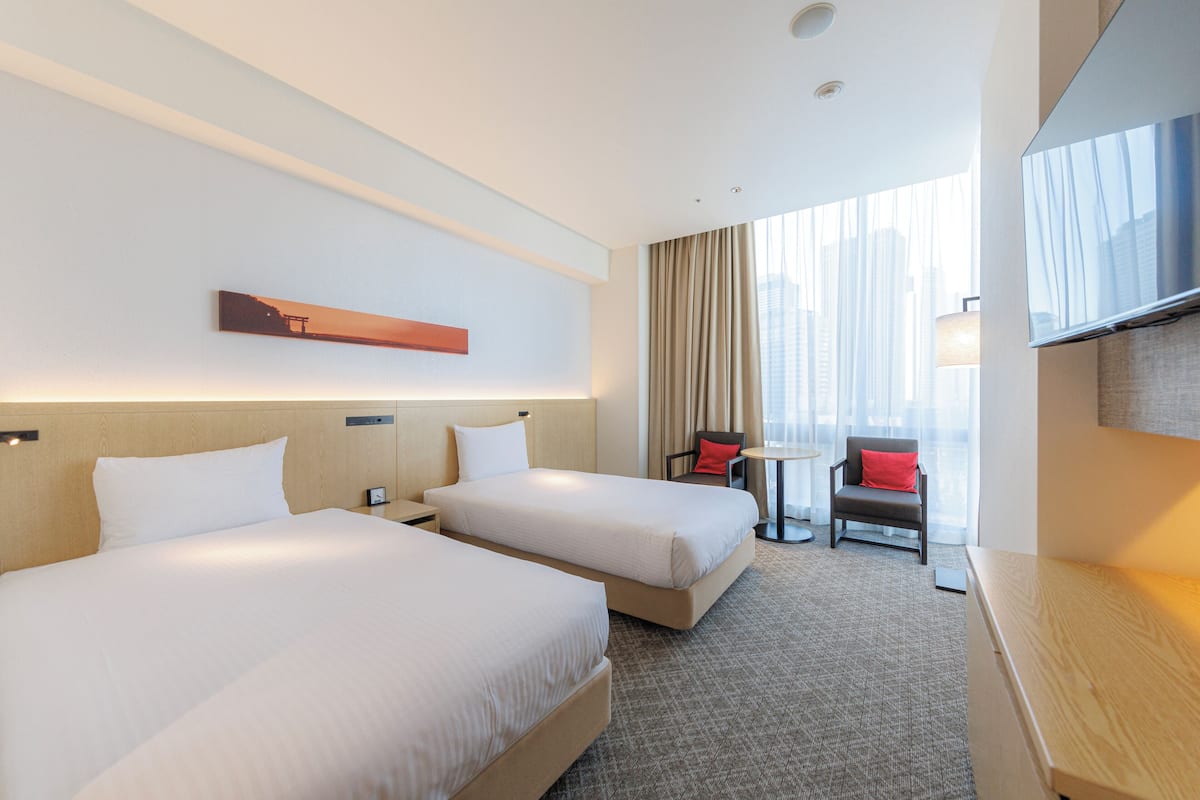 A hotel room with two beds, a TV, a small table, and a chair.