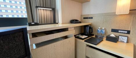 A modern hotel room with a wooden desk, a telephone, a coffee maker, and a small shelf with cups and a tissue box.
