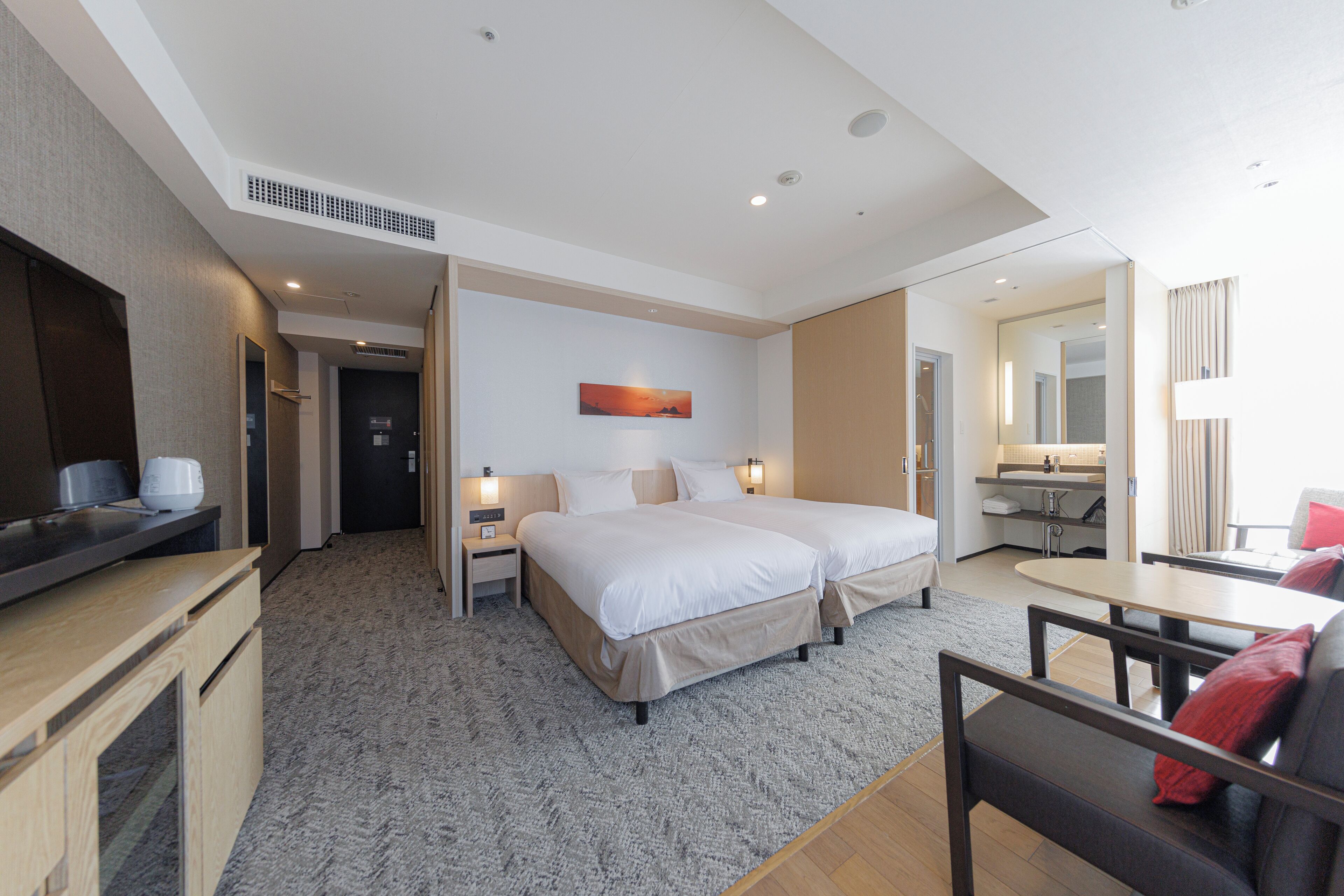 A modern hotel room with a large bed, bedside tables, a desk, and a small seating area.