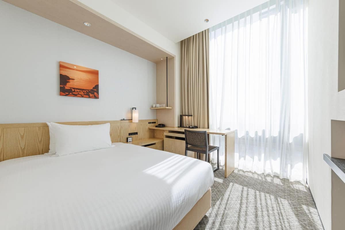 A hotel room with a bed, desk, chair, and a TV.