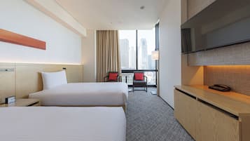 A hotel room with two beds, a desk, a TV, and a window with a city view.