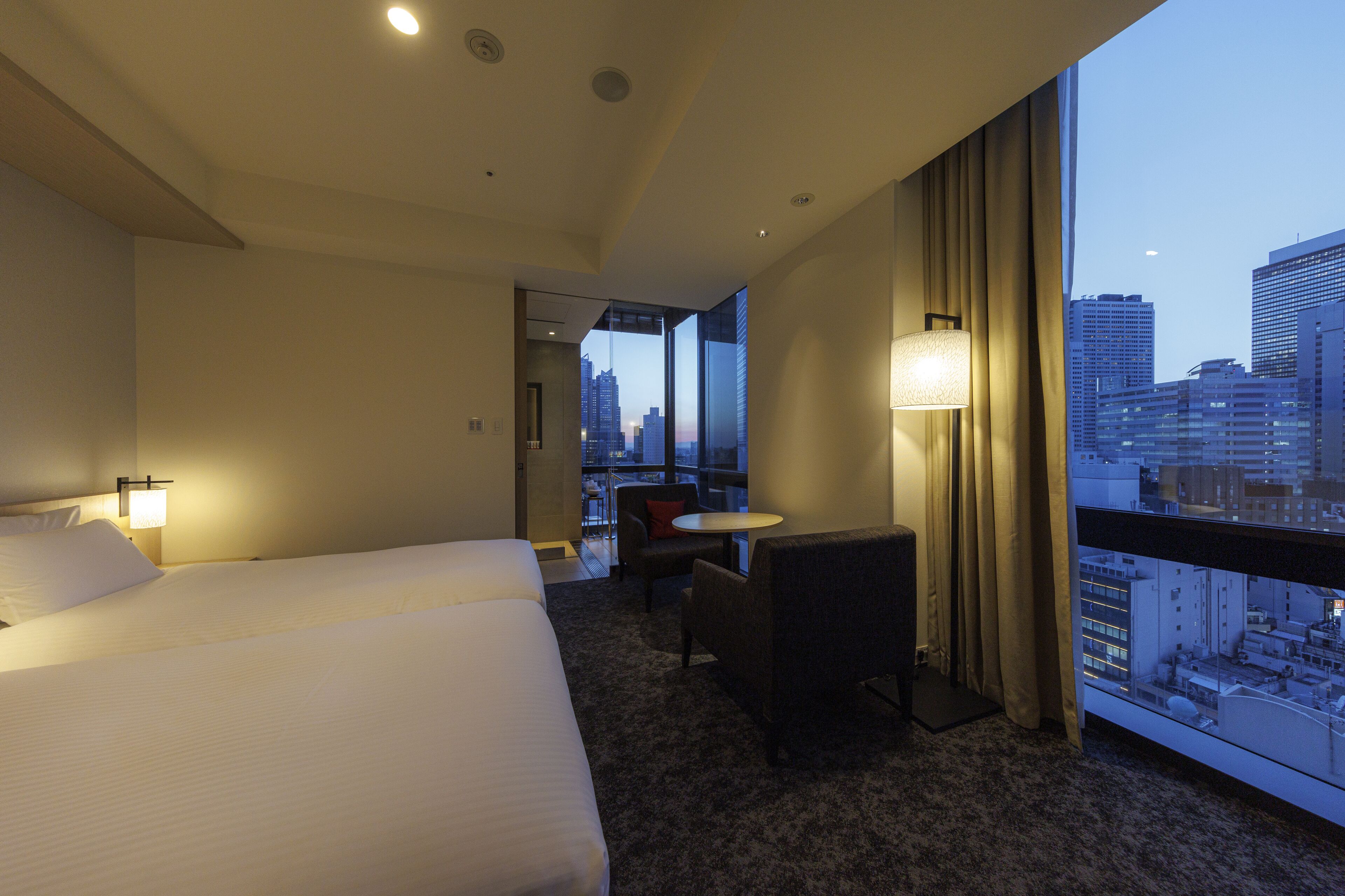 Une chambre d’hôtel avec un grand lit, une petite table, une chaise et une vue sur le paysage urbain.