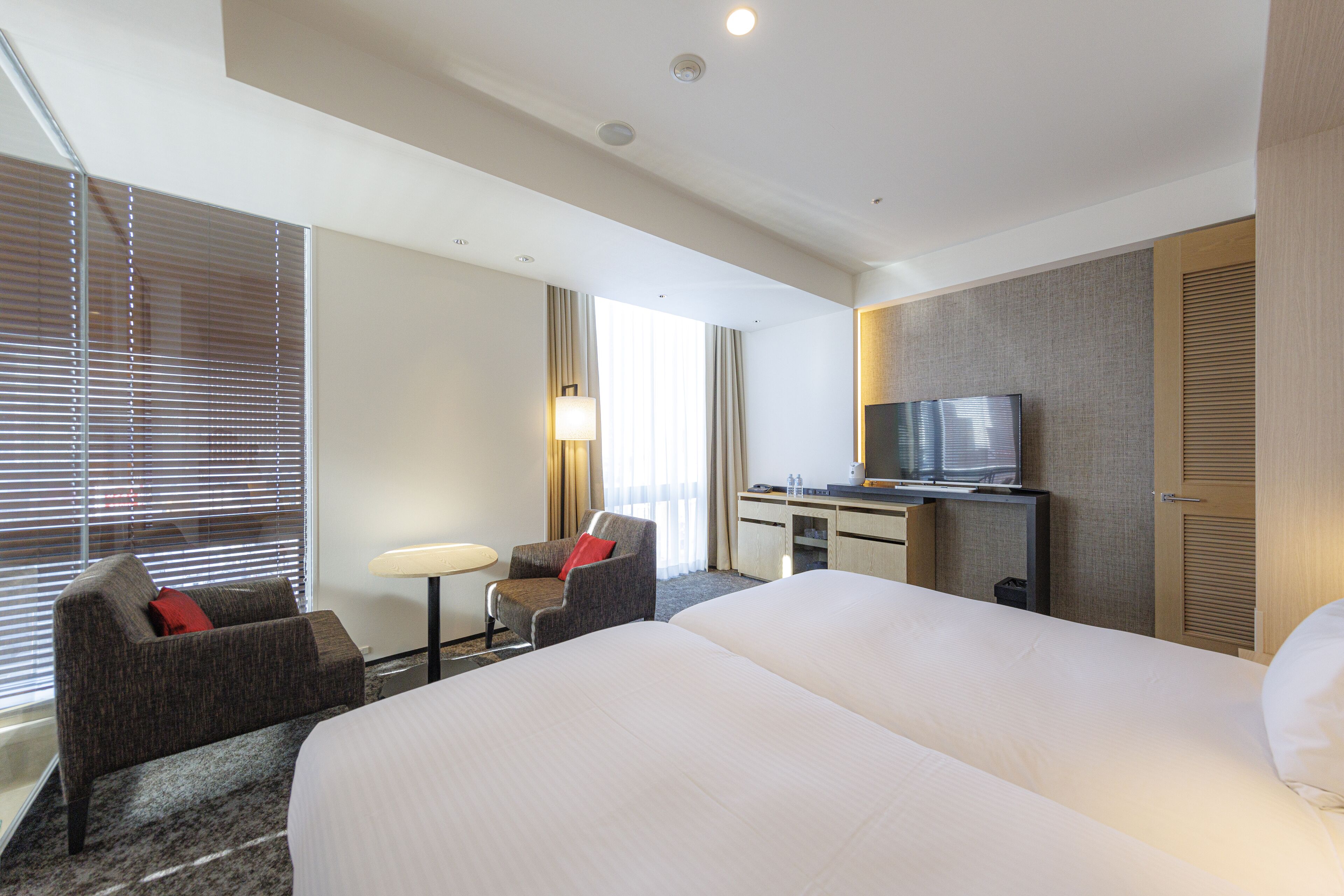A hotel room with a large bed, a desk with a TV, a chair, and a small table.