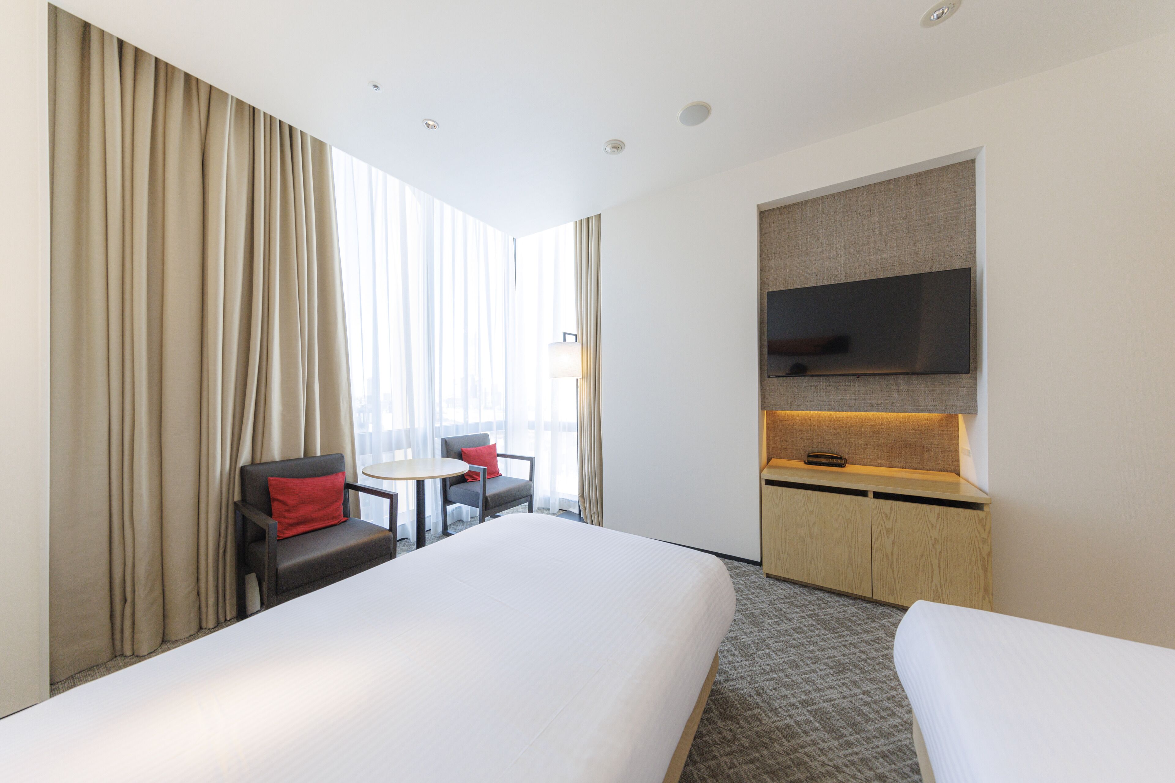 Une chambre d’hôtel avec un grand lit, un bureau avec une chaise, un téléviseur fixé au mur et une fenêtre avec des rideaux.