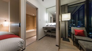 A hotel room with a bed, a bathroom, a seating area with a view of the city.