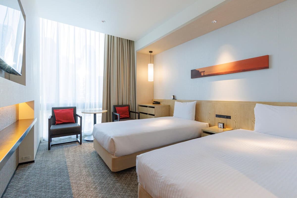 A hotel room with two beds, a desk, a chair, a small table, and a window with curtains.