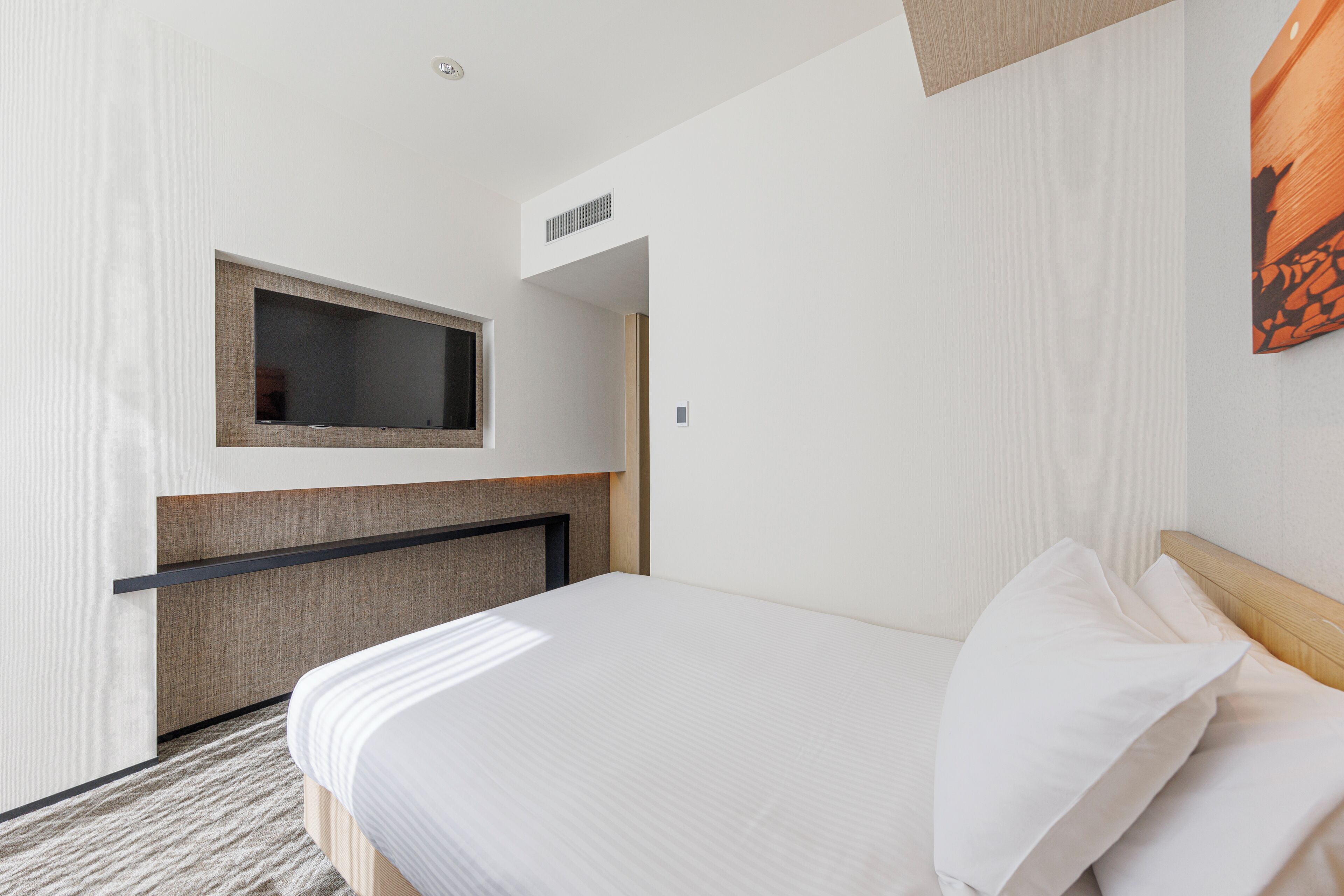 A hotel room with a bed, a TV mounted on the wall, and a small window.