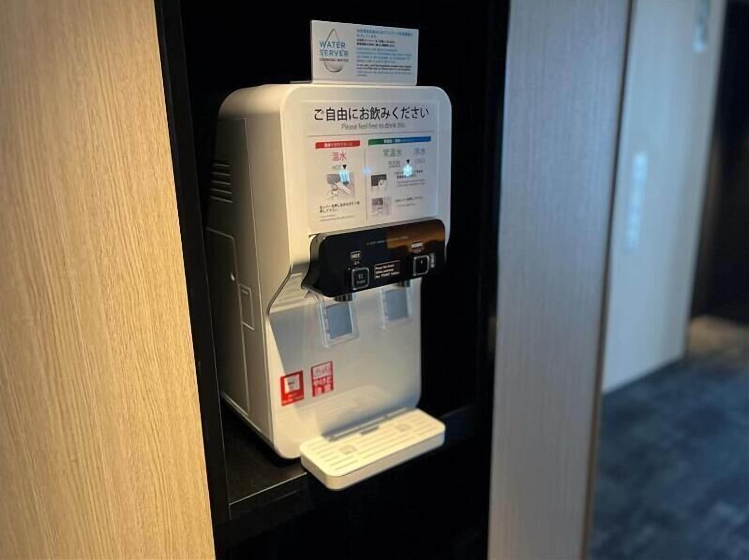 A water dispenser with a sign in Japanese and English, a button, and a water bottle holder.