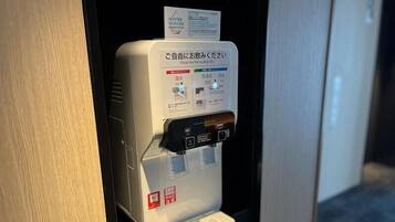 A water dispenser with a sign in Japanese and English, a button, and a water bottle holder.