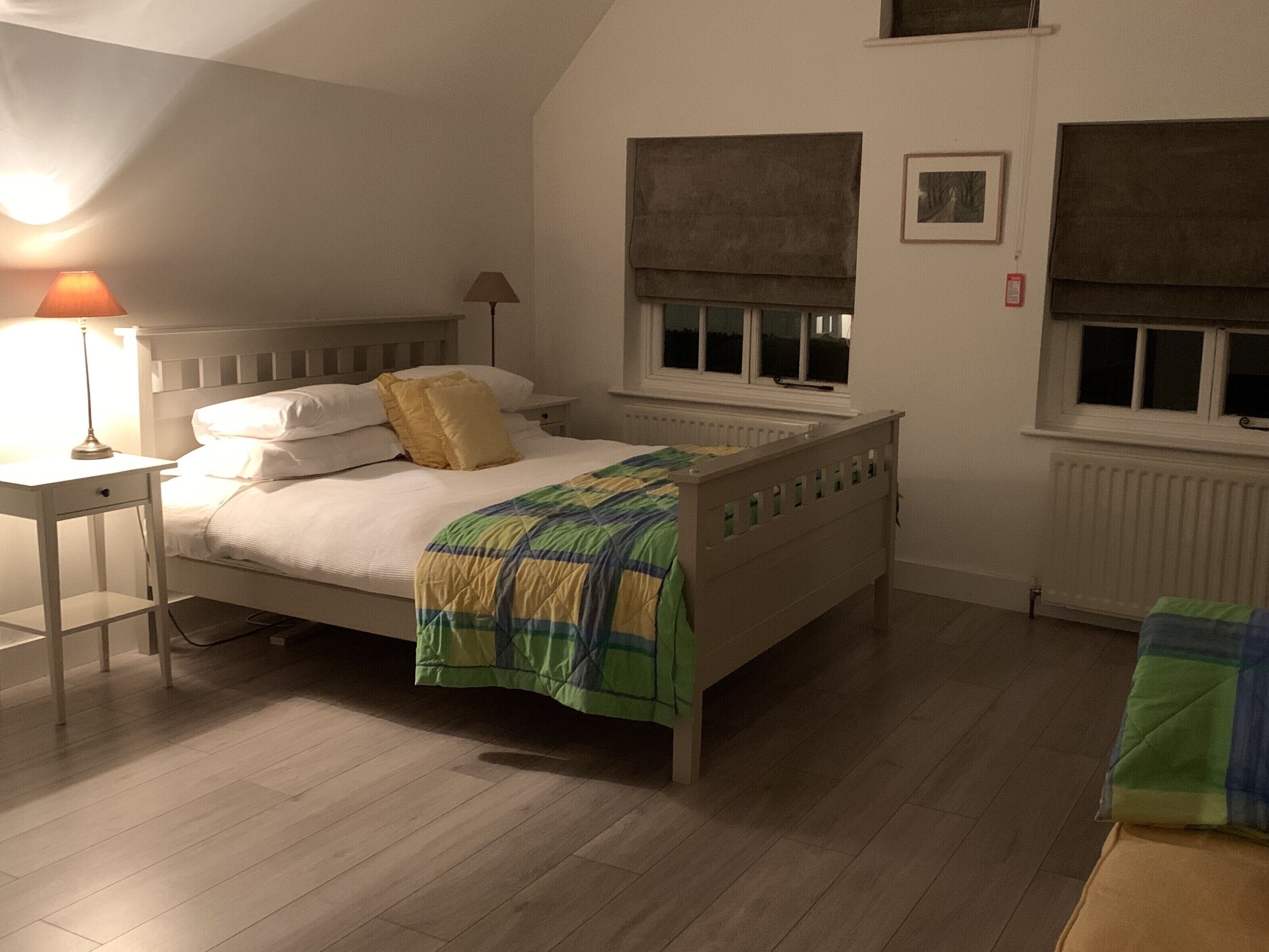 Un dormitorio con cama, mesita de noche, lámpara, ventana con persiana y radiador.