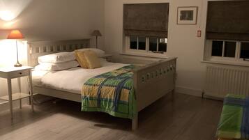 Un dormitorio con cama, mesita de noche, lámpara, ventana con persiana y radiador.