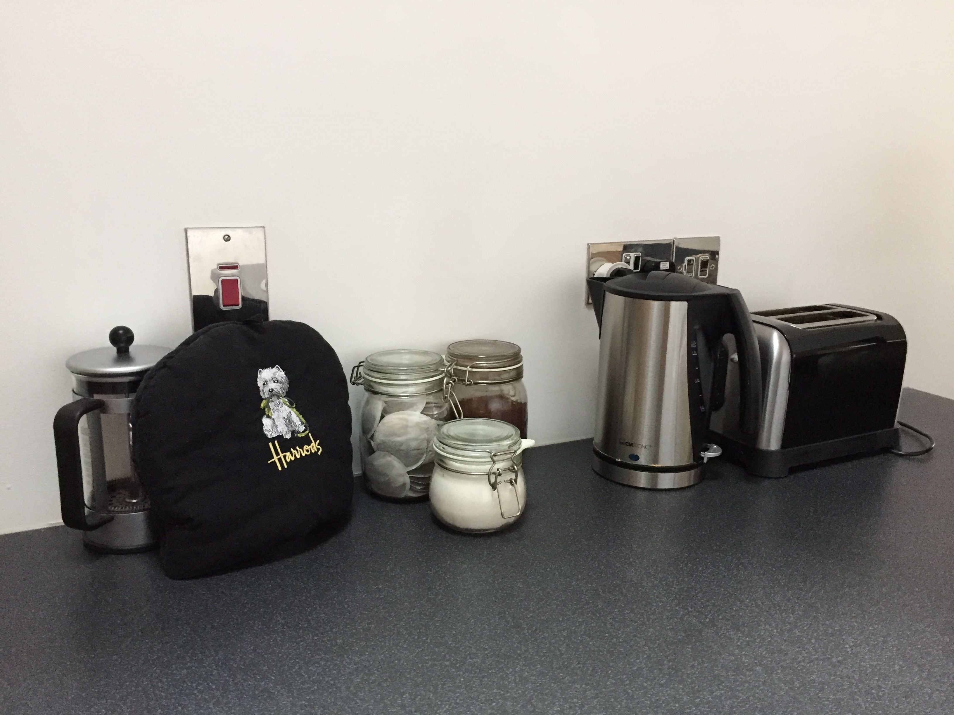 A kitchen counter with a coffee maker, toaster, jars, and a black bag with a dog illustration.
