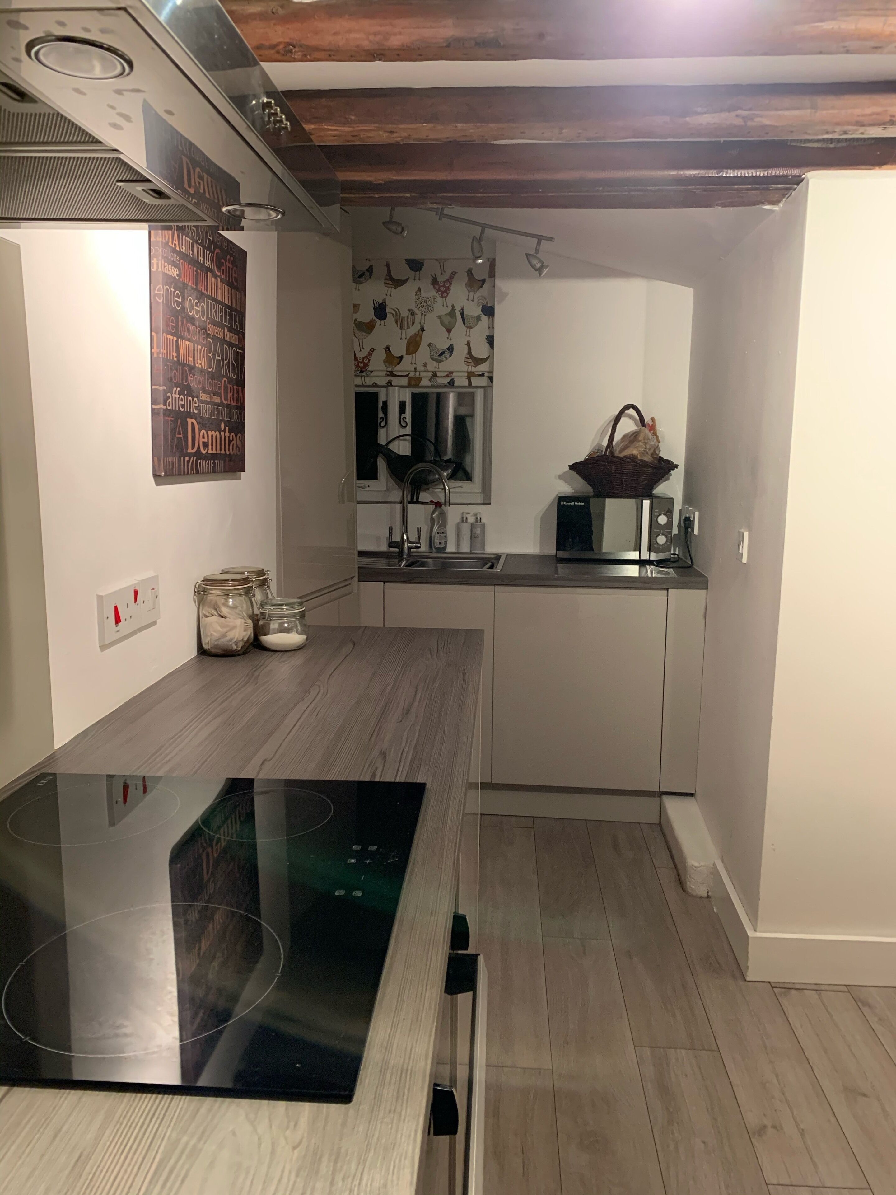 A modern kitchen with a black induction cooktop, white cabinets, and a wooden floor.
