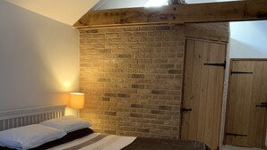 A bedroom with two beds, a brick wall, wooden doors, and a sloped ceiling. - Appletree Cottages (Bury St Edmunds)