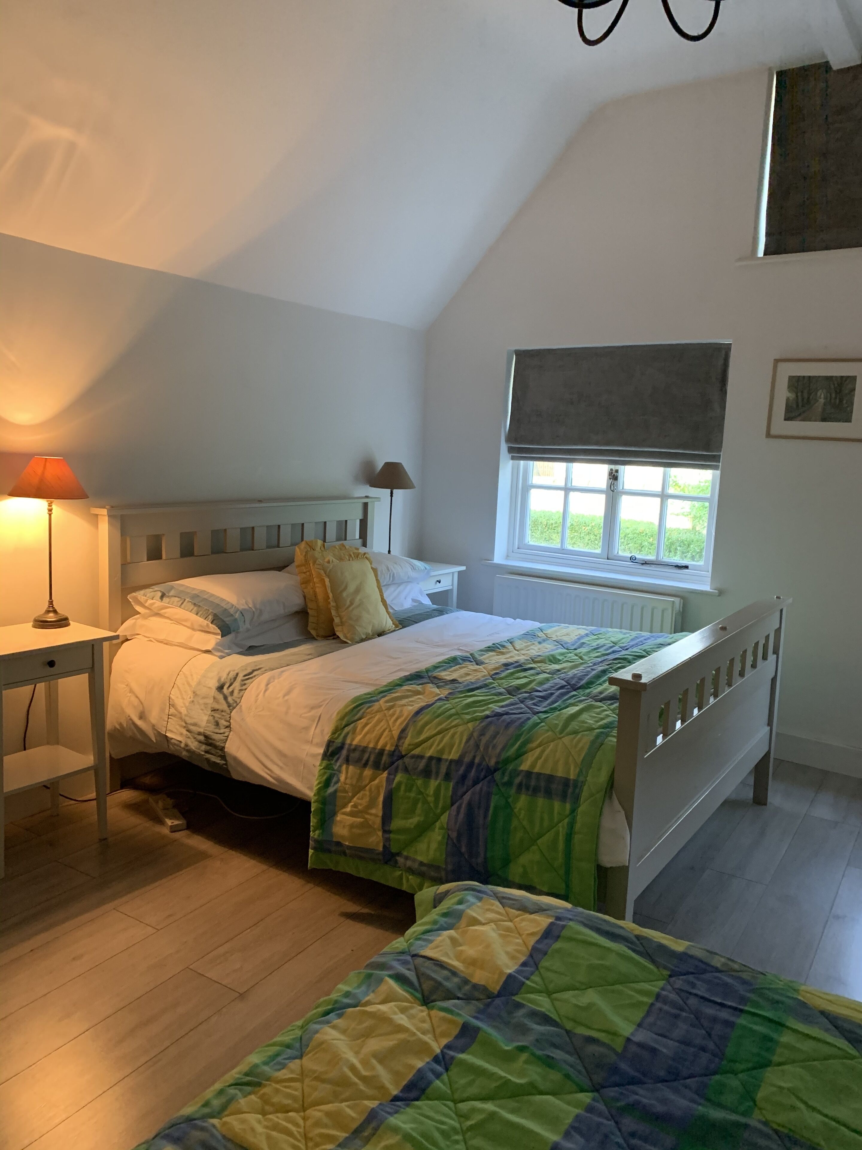 Et soveværelse med seng, natbord, lampe, vindue og udsigt til grønne omgivelser.
