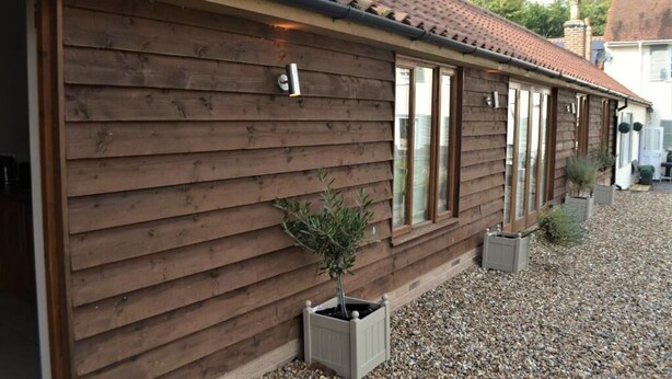 A wooden building with a tiled roof, large windows, and a small tree in a planter. - Appletree Cottages (Bury St Edmunds)