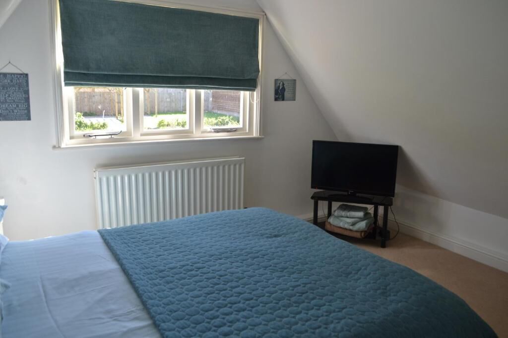A bedroom with a bed, a television on a stand, a window with a green blind, and a radiator.