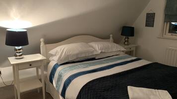A bedroom with a bed, two bedside tables, a lamp on each table, a quilted bedspread, and a wall with a framed quote.