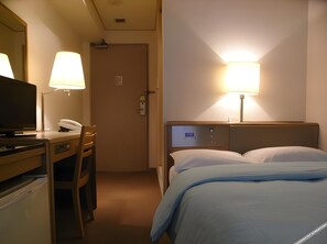 Una habitación de hotel con una cama, un escritorio con teléfono, un televisor y dos lámparas.