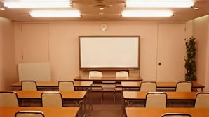 Une salle de conférence équipée d’un tableau blanc, de bureaux, de chaises et d’une horloge au mur.