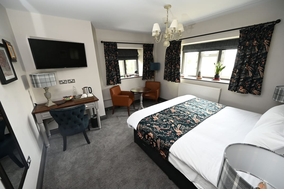Habitación de hotel con cama, escritorio con silla, televisor y ventana con cortinas.