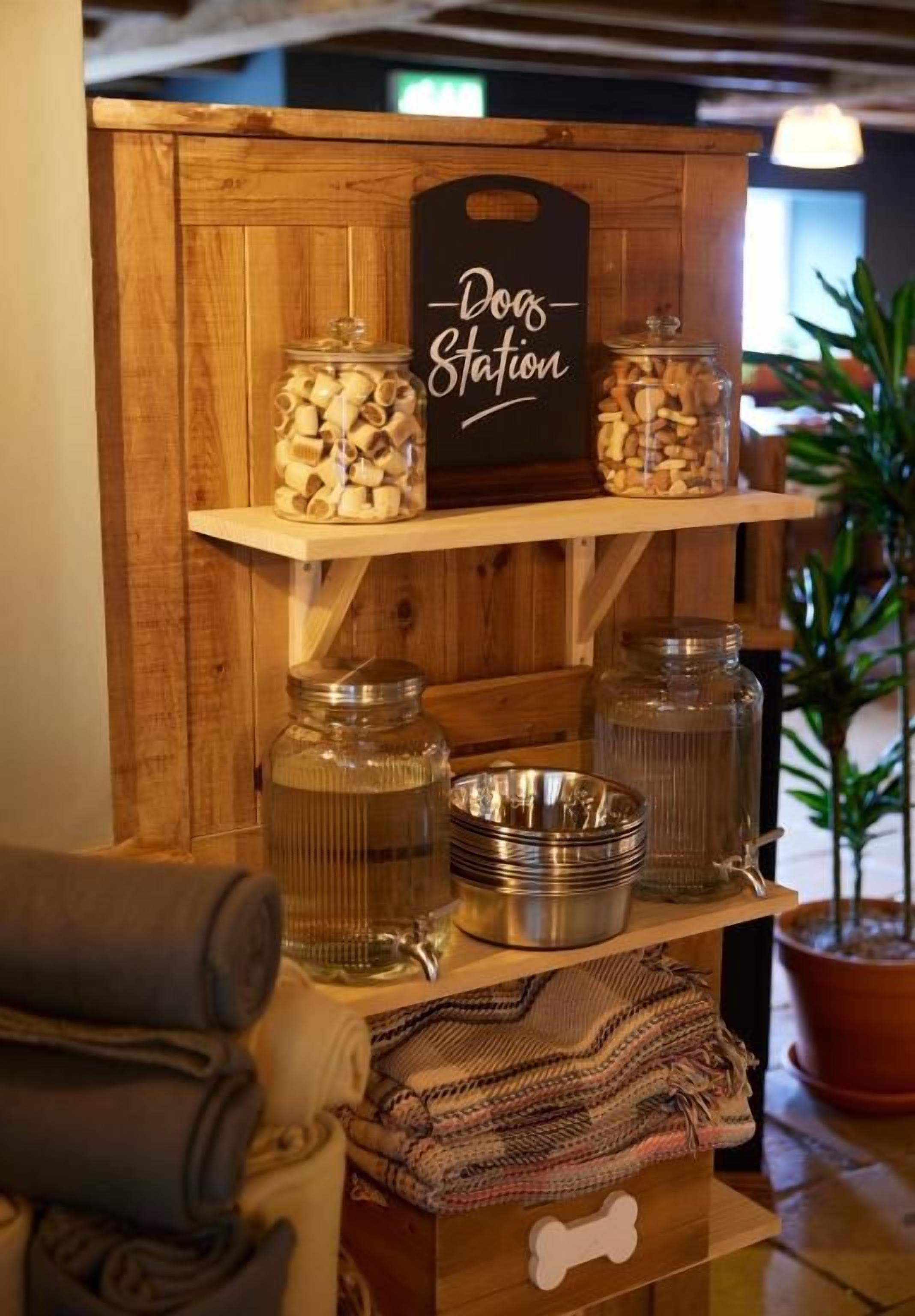 Un espositore in legno con barattoli e ciotole, un cartello con scritto 'Dogs Station' e un cassetto a forma di osso.