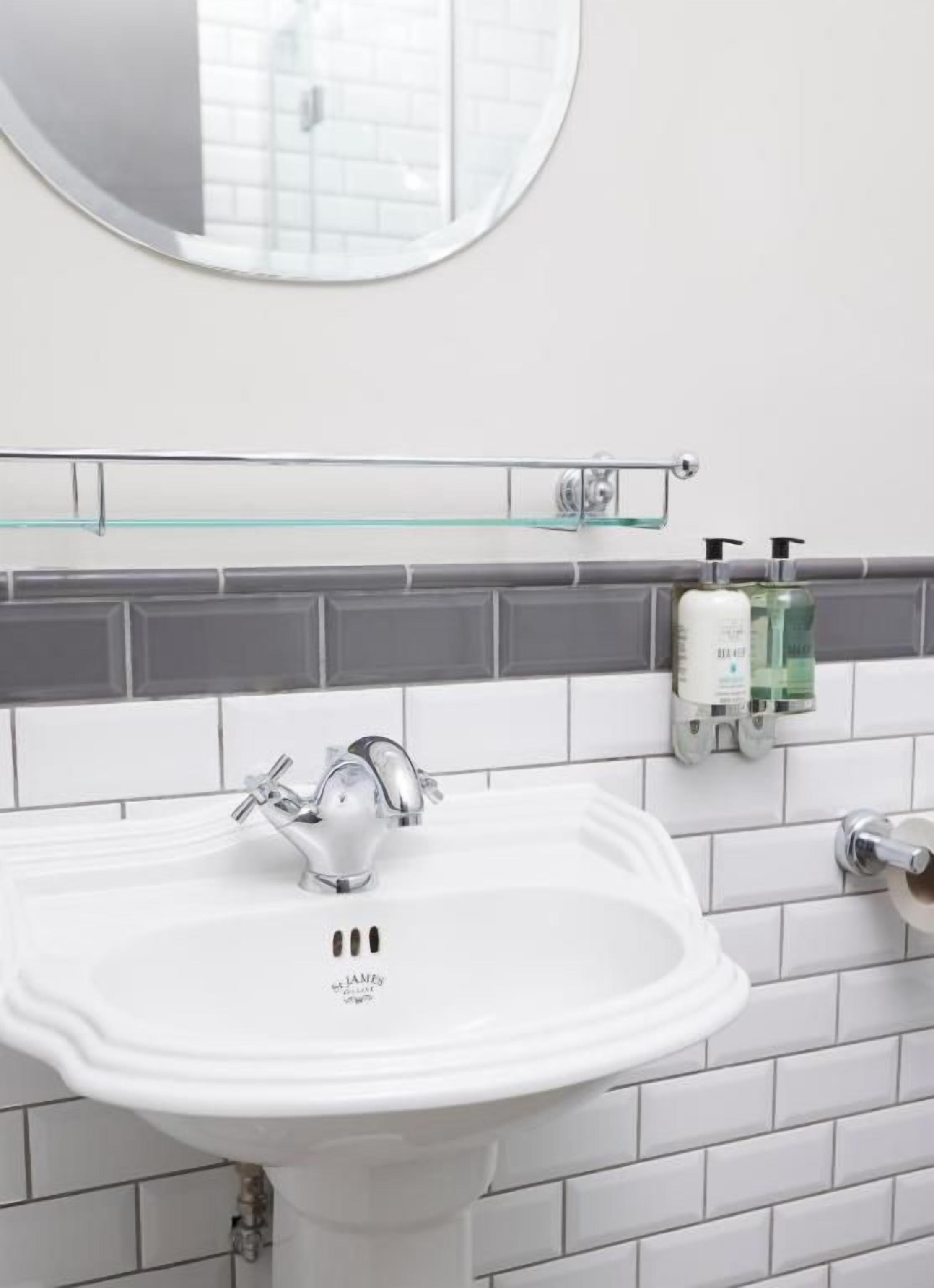 Un baño con un lavamanos blanco, un espejo encima y una repisa de vidrio sobre el lavamanos.