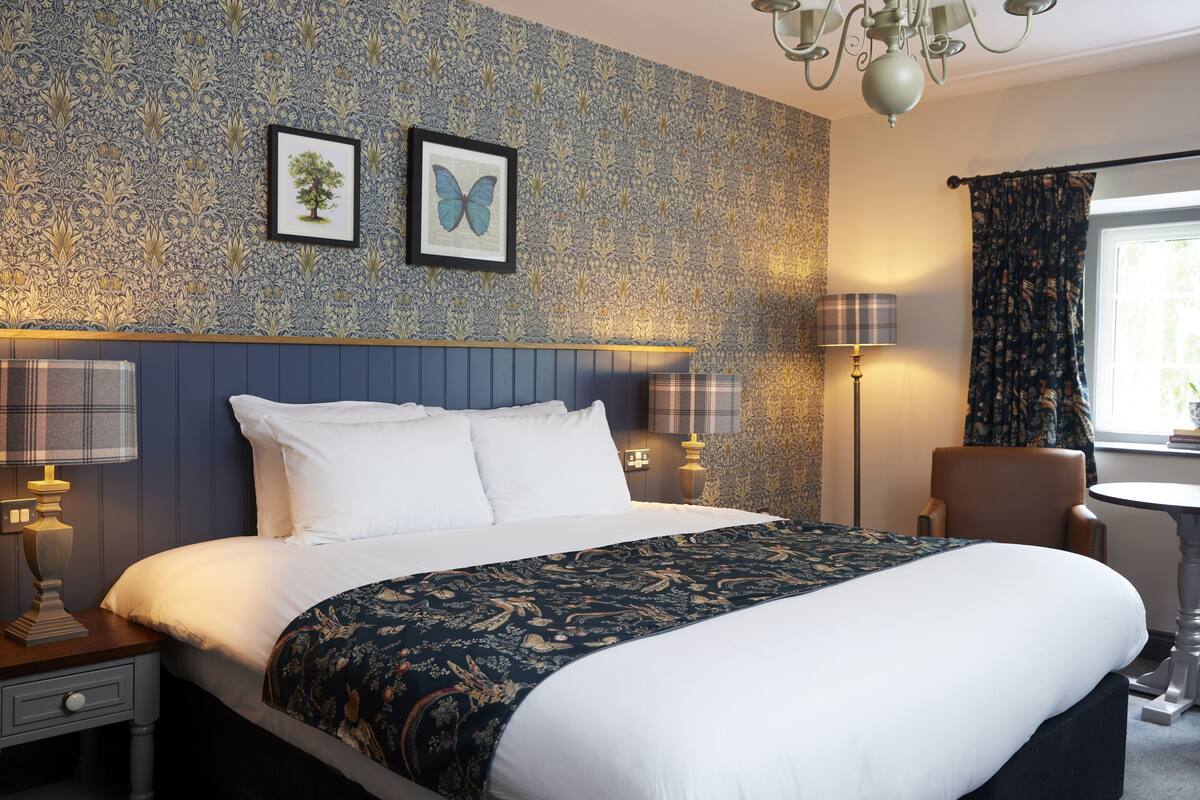 Habitación de hotel con una cama grande, una silla, una mesa y un ventanal con cortinas.