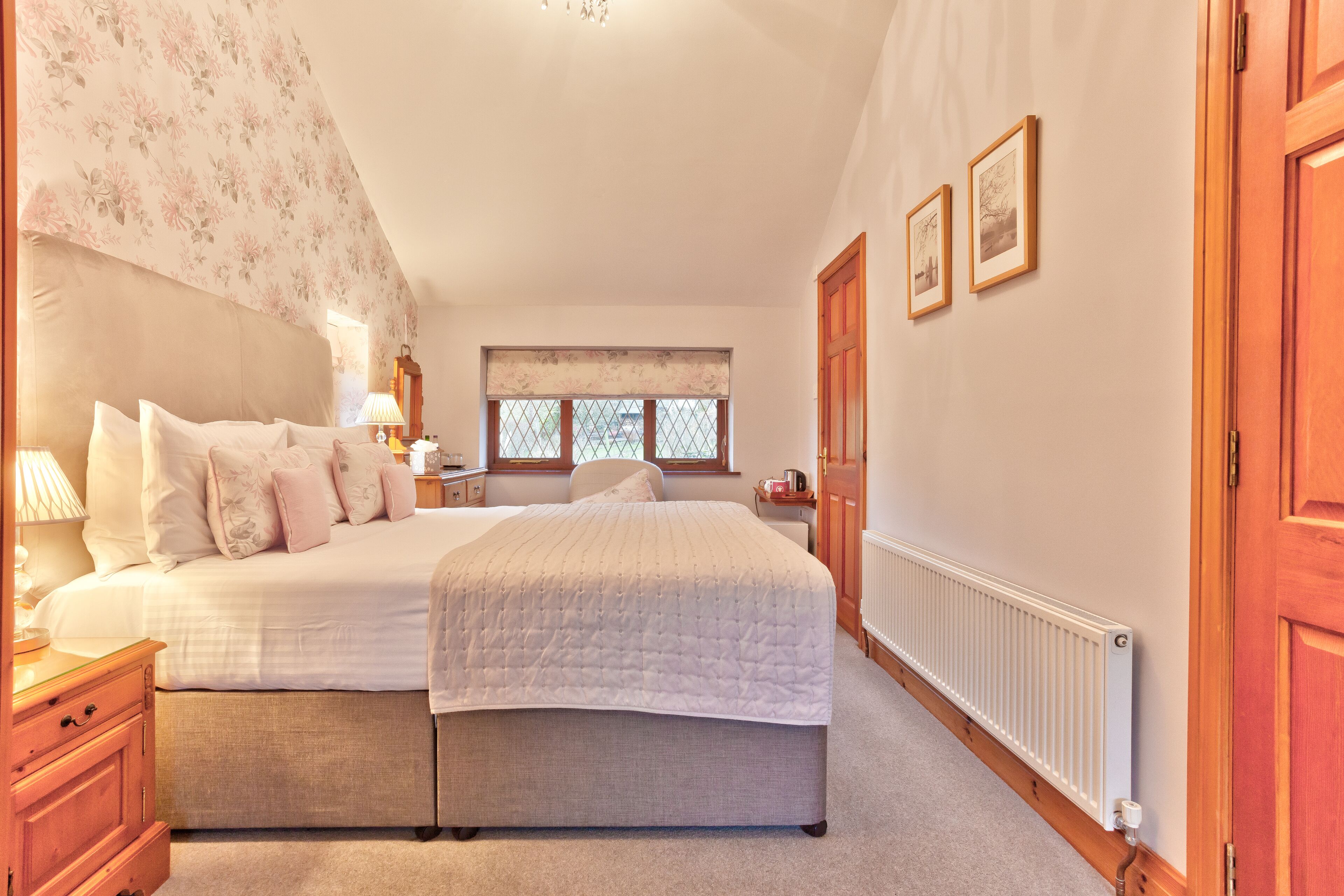 A bedroom with a large bed, a nightstand, a dresser, a window with a view, and a radiator.