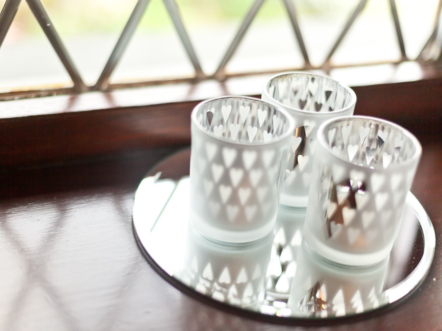 Three glass candle holders with heart cutouts on a reflective tray.